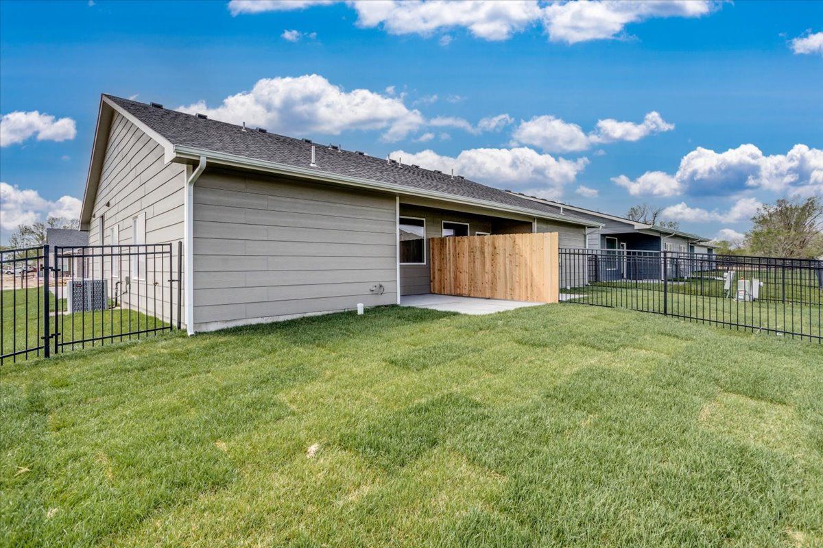 The backyard of a house with a fence and a large lawn.