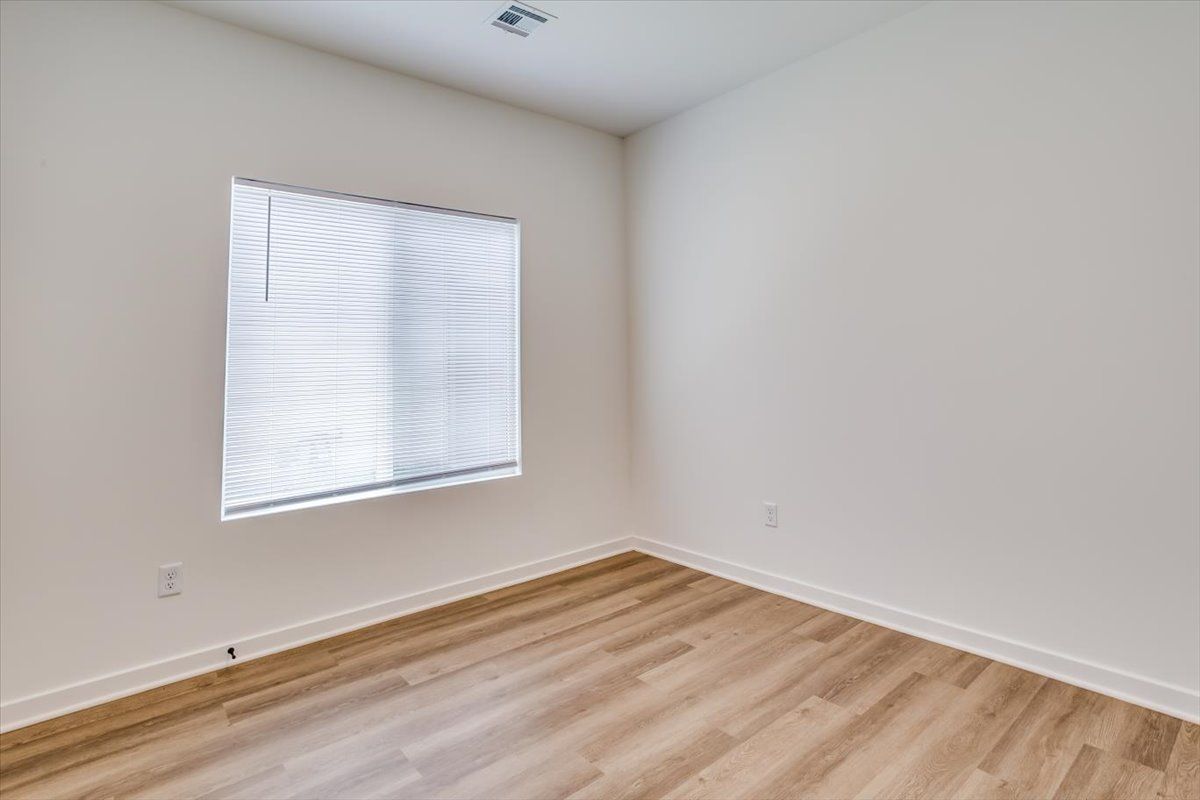 An empty bedroom with hardwood floors and a window.