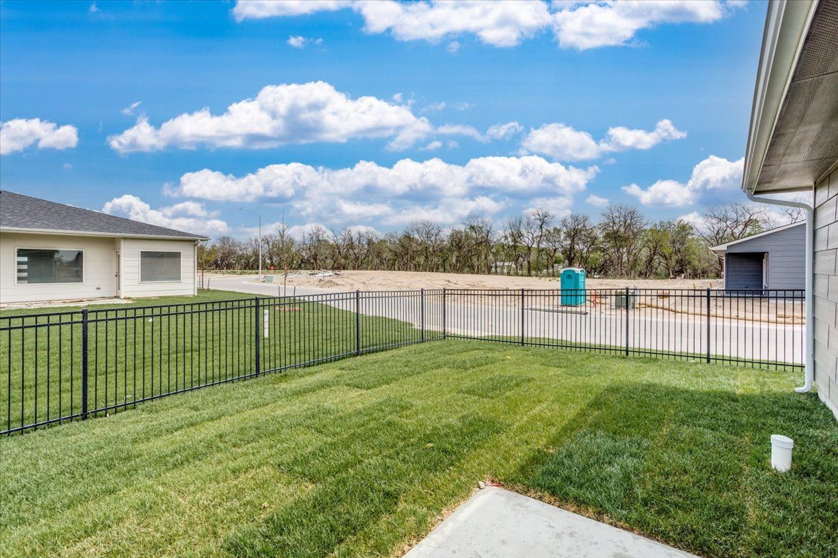 A fenced in backyard with a lush green lawn and a house in the background.