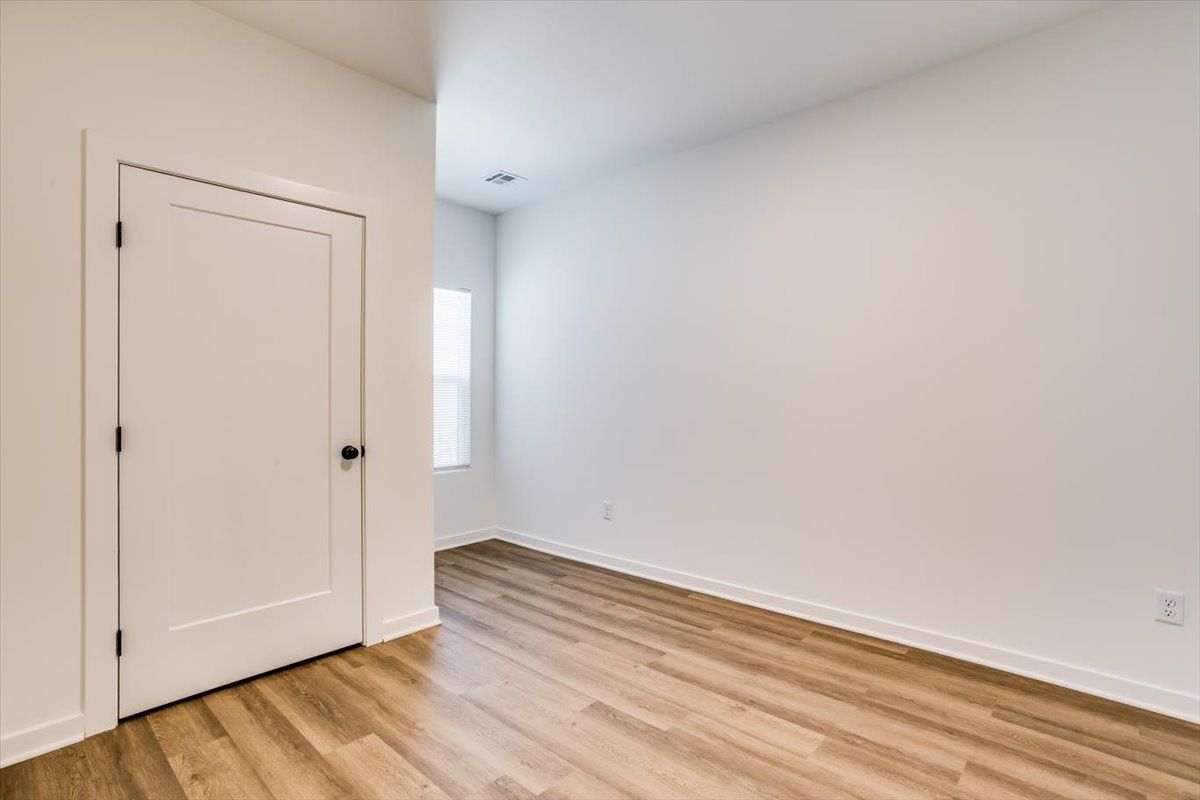 An empty bedroom with hardwood floors and white walls.