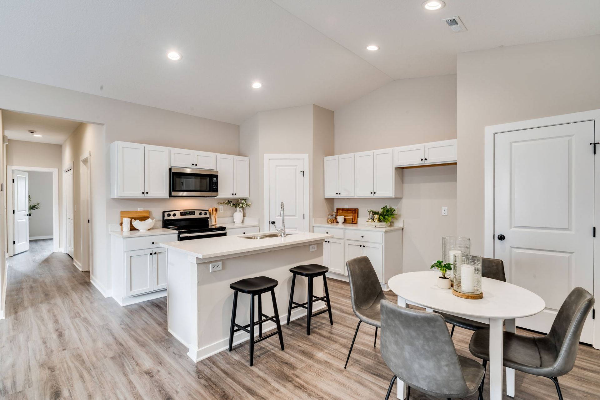 A kitchen with white cabinets , stainless steel appliances , a table and chairs.