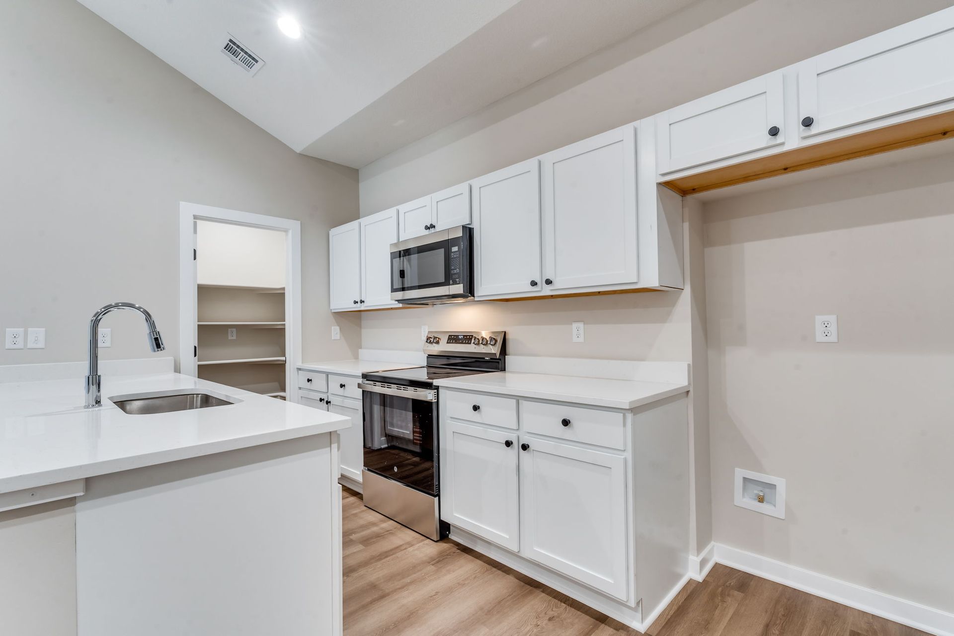 A kitchen with white cabinets , stainless steel appliances , a sink , and a microwave.