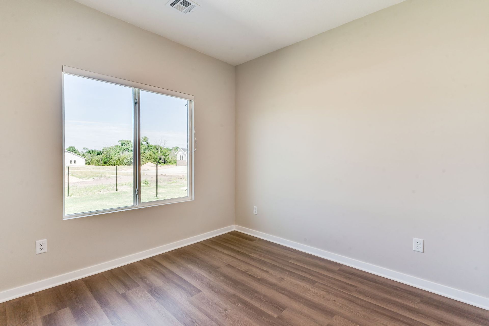 An empty bedroom with hardwood floors and a large window.