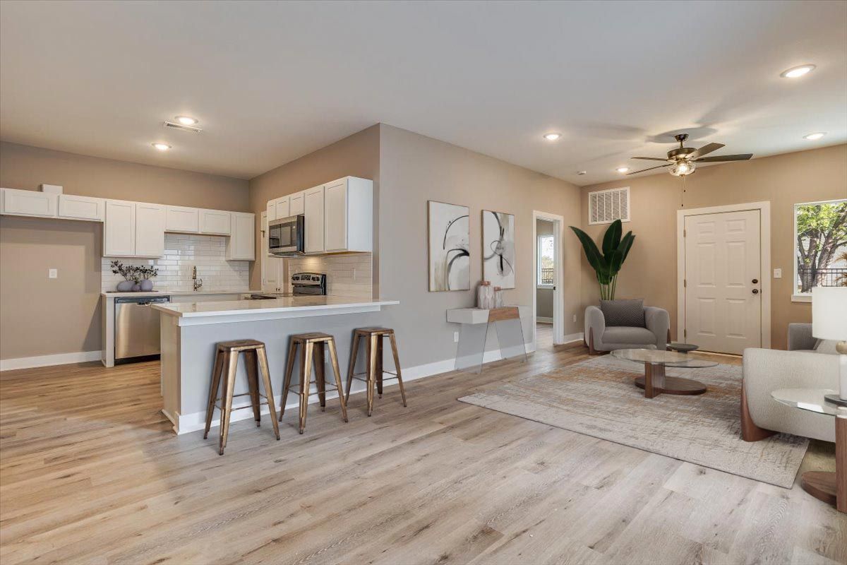 A living room with hardwood floors , a kitchen and a ceiling fan.