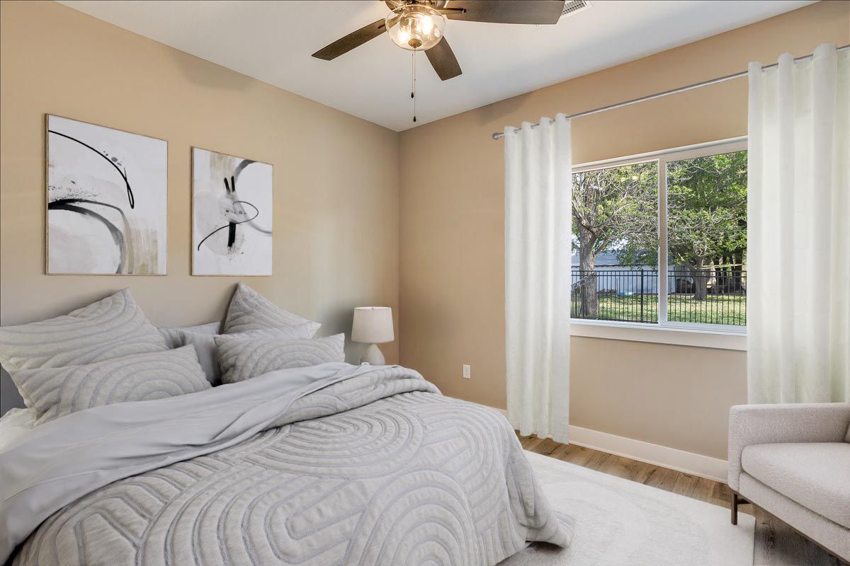 A bedroom with a bed , chair , ceiling fan and window.