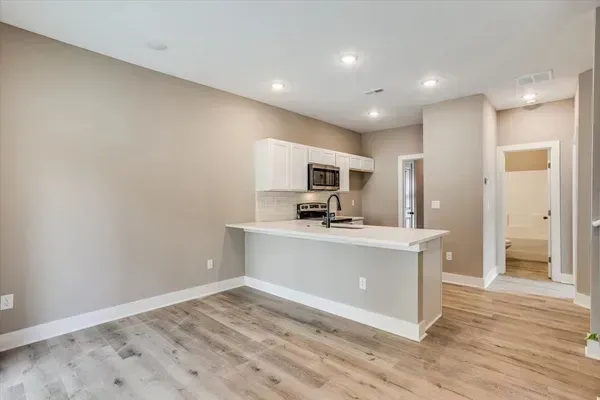 A living room with hardwood floors and a kitchen in the background.