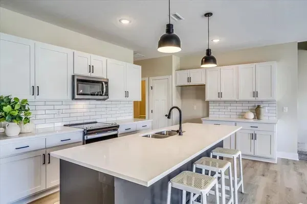 A kitchen with white cabinets , stainless steel appliances , and a large island.