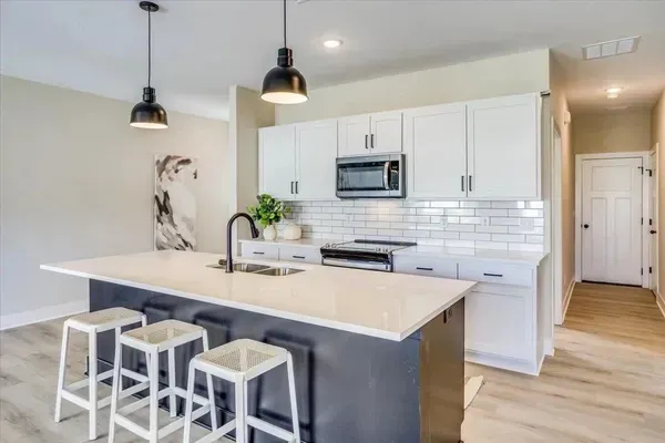 A kitchen with white cabinets and stools and a large island.