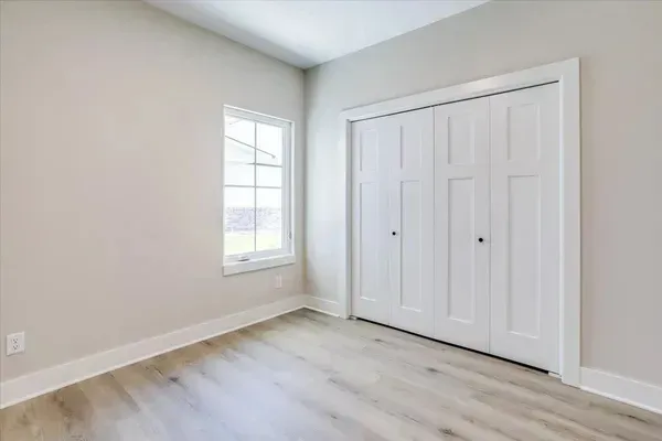 An empty bedroom with hardwood floors , white walls , and a window.