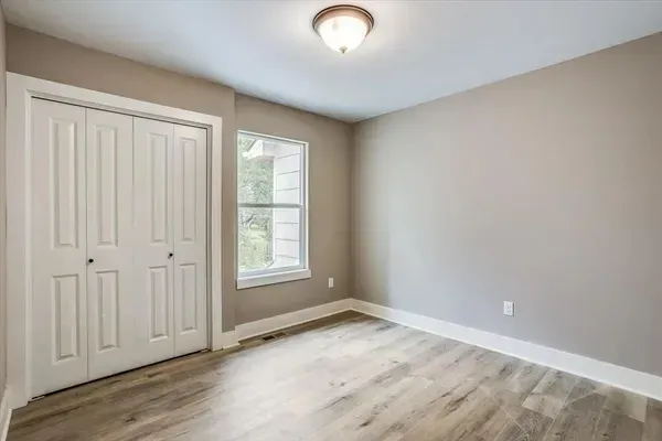 An empty bedroom with hardwood floors and a window.
