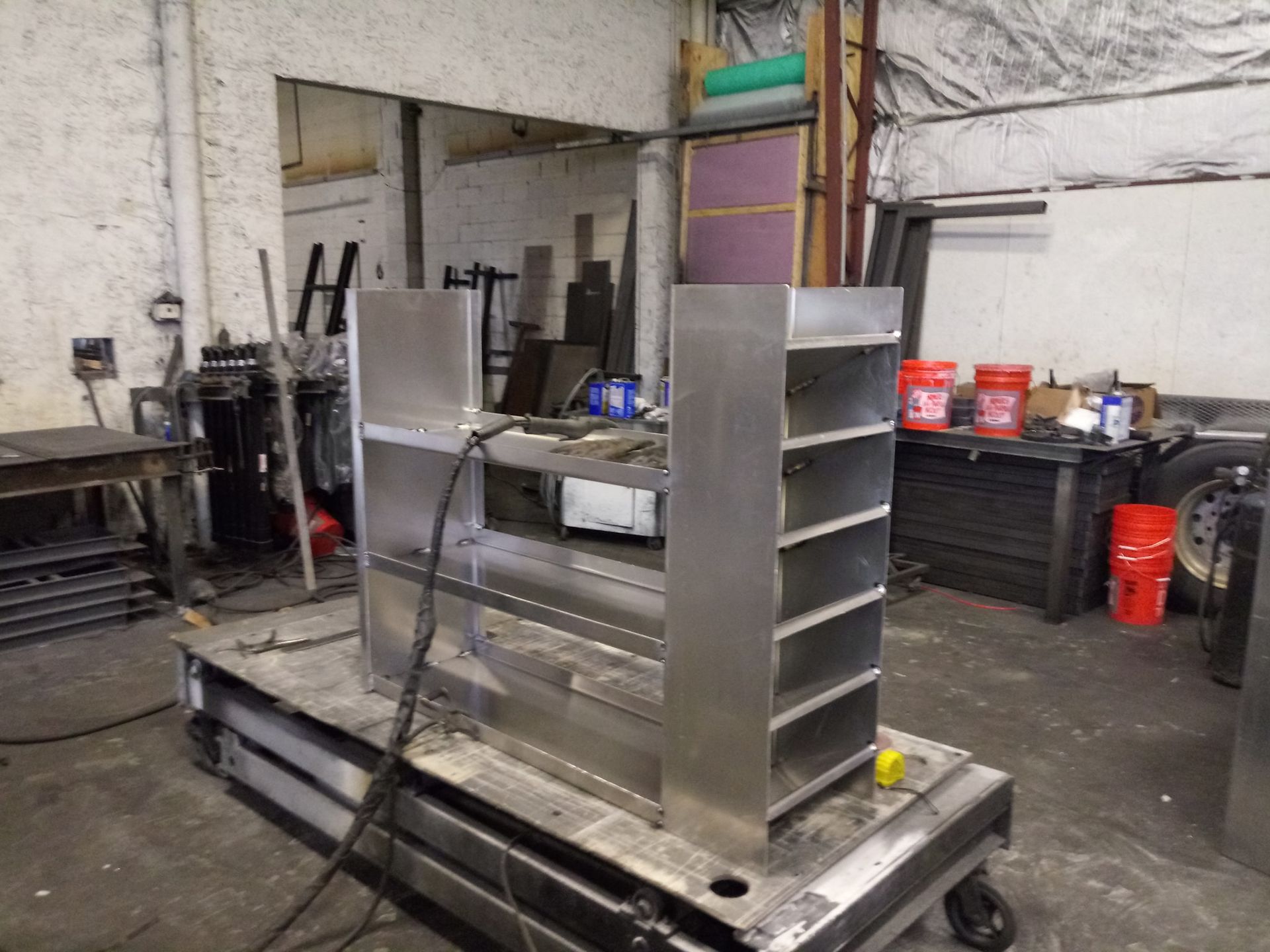 A stainless steel shelf is sitting on top of a cart in a workshop.