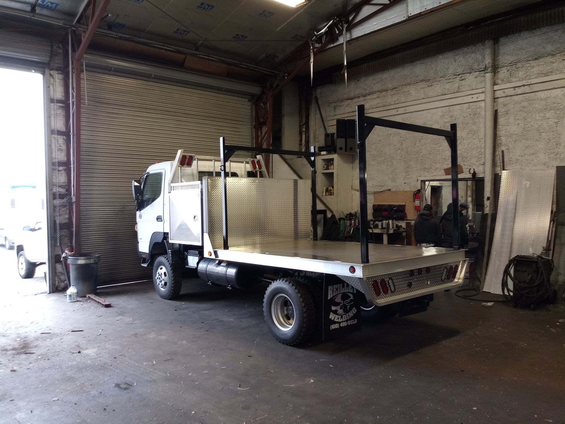 A white truck with a flat bed is parked in a garage.