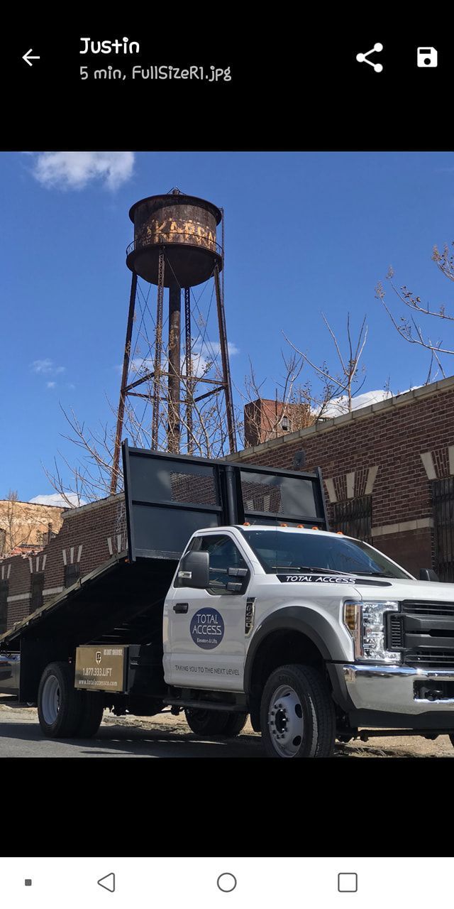 A white tow truck is parked in front of a water tower.
