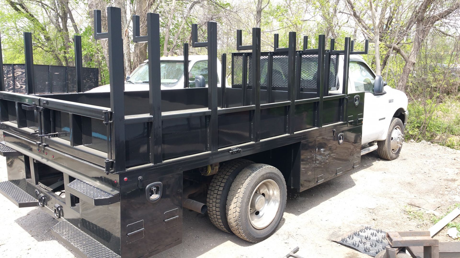 A white truck with a black bed is parked in a gravel lot.