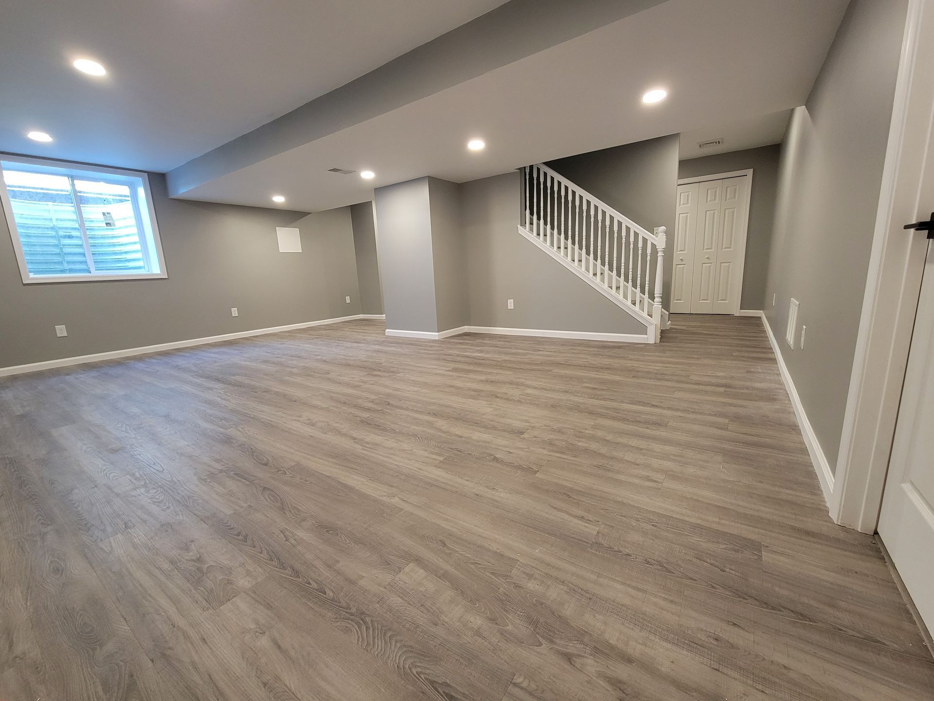 Finished basement with gray walls, wood-look flooring, and a white staircase.