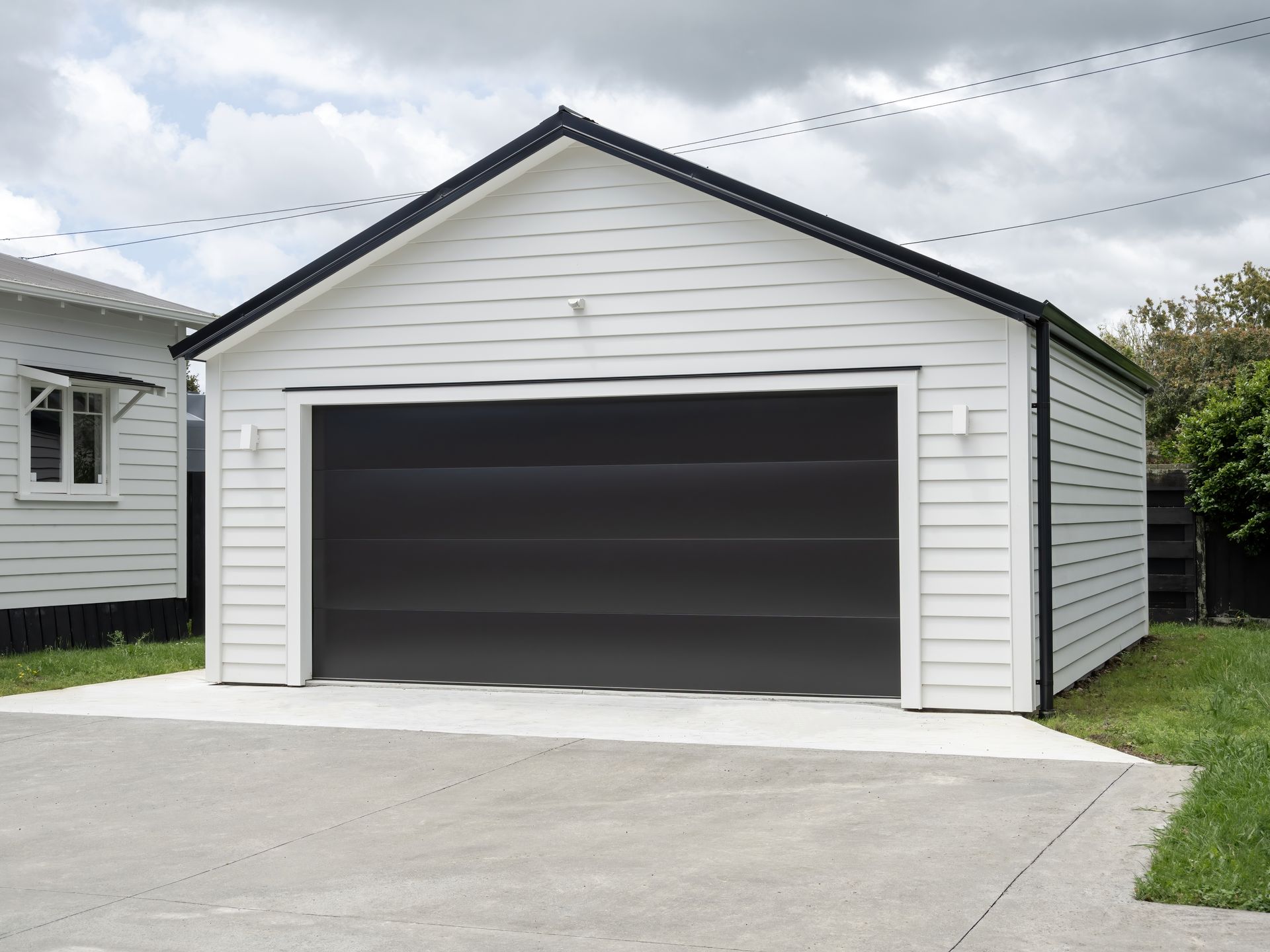 White garage with black door, black trim, and concrete driveway against a cloudy sky.