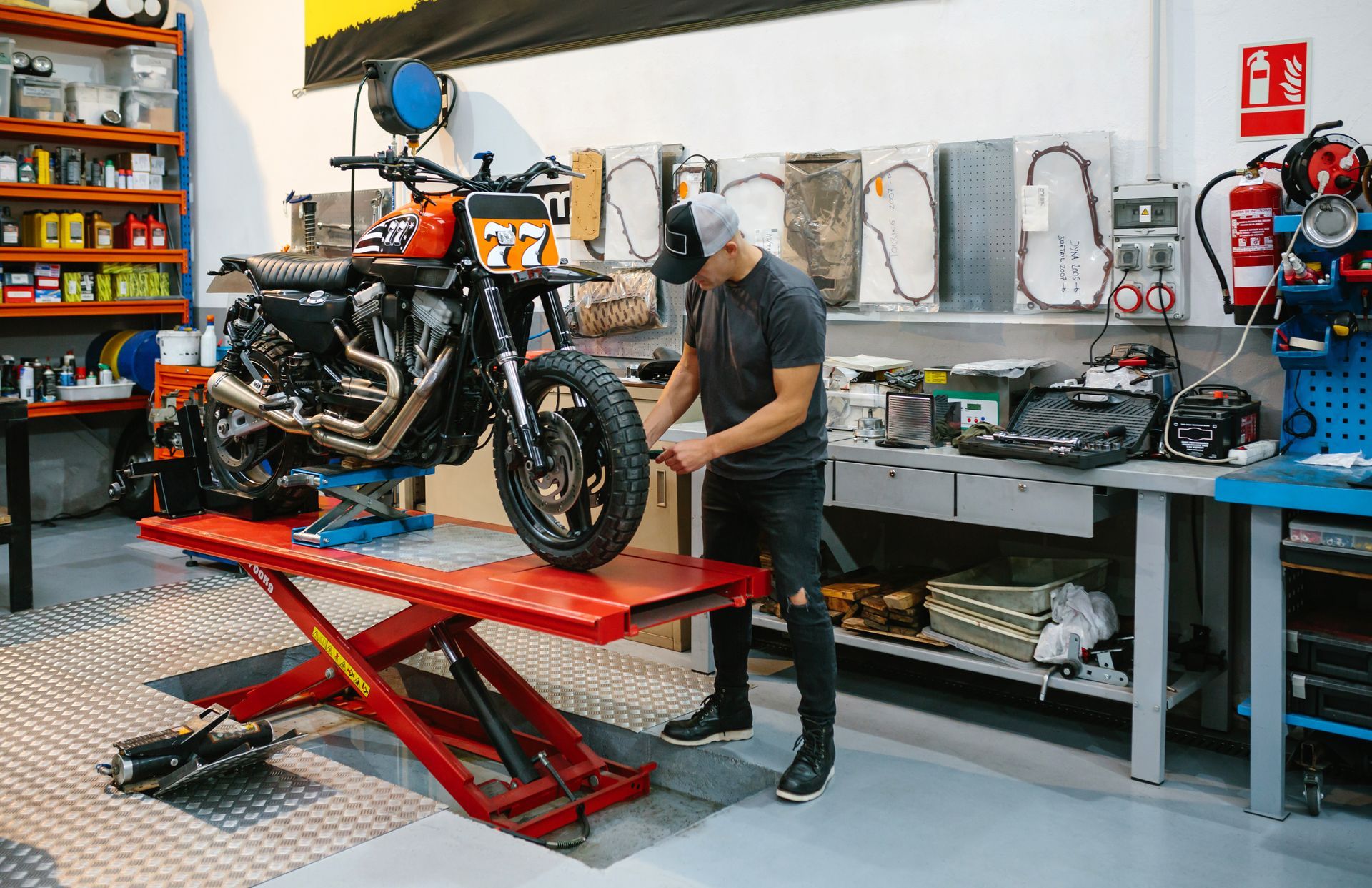 Man working on a motorcycle in a shop. The bike is on a lift, and the mechanic is adjusting the front wheel.