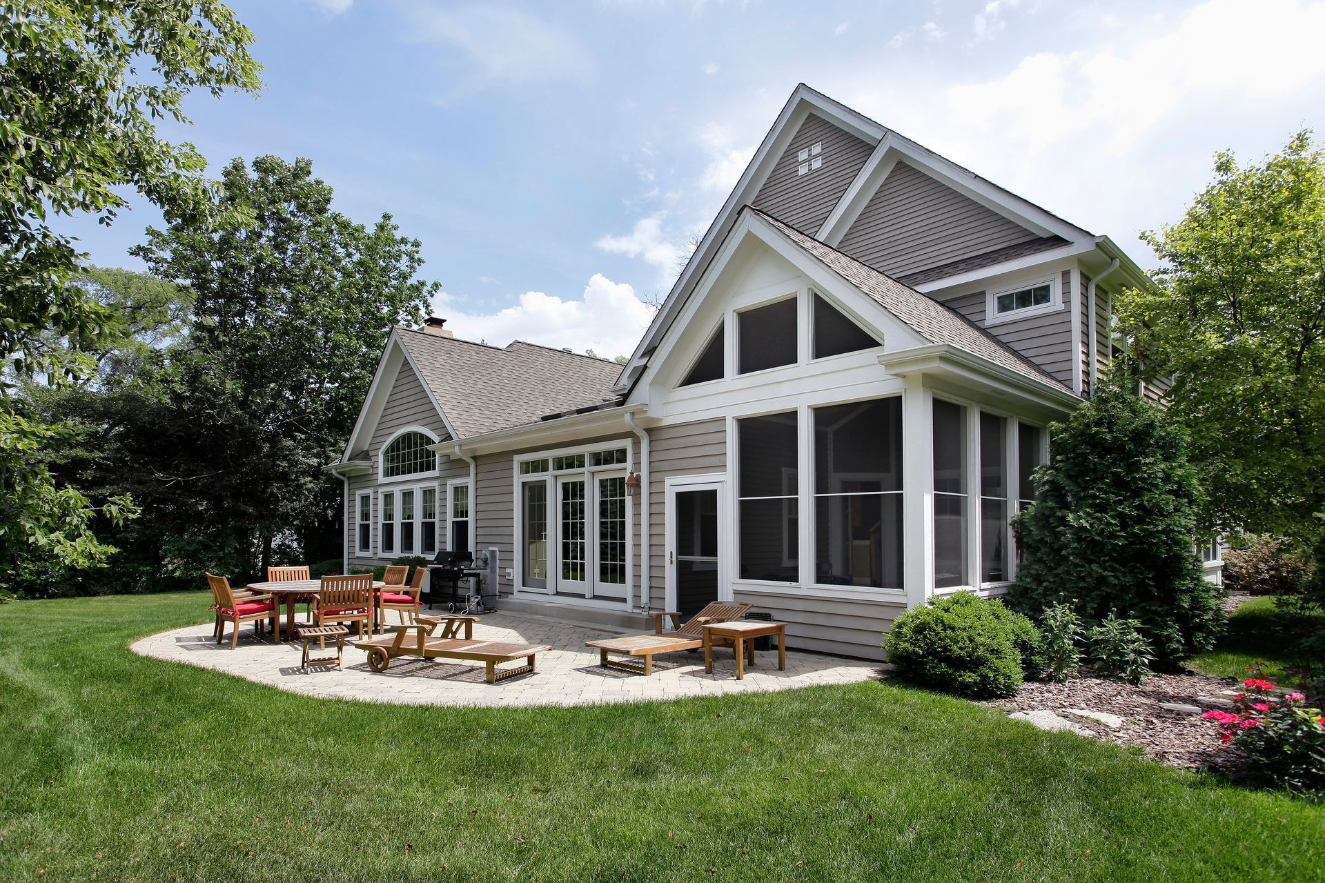 A home with a screened porch and patio with seating surrounded by a grassy yard.