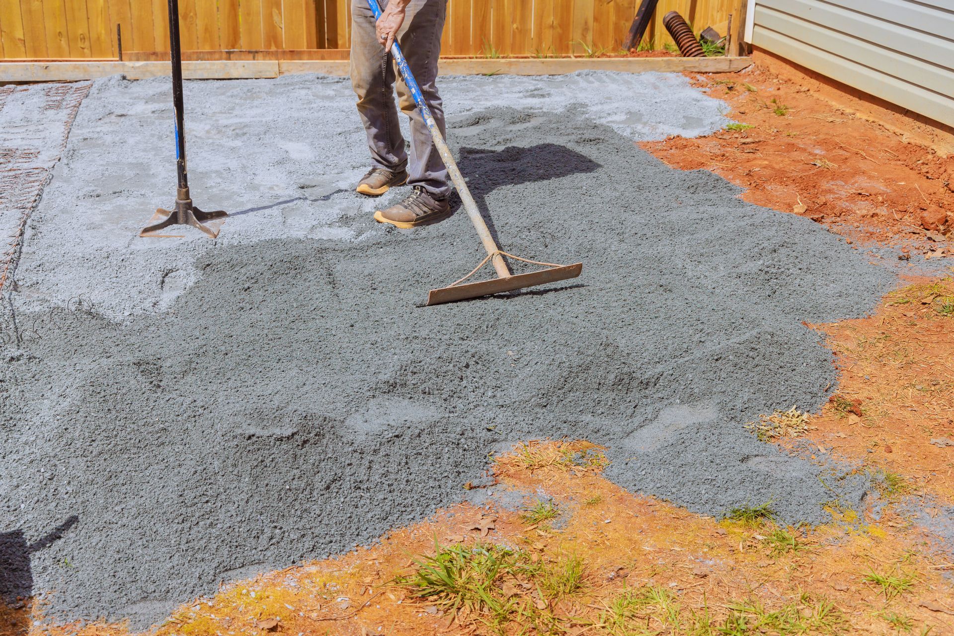 Person leveling crushed stone base with a rake on a patio construction site.