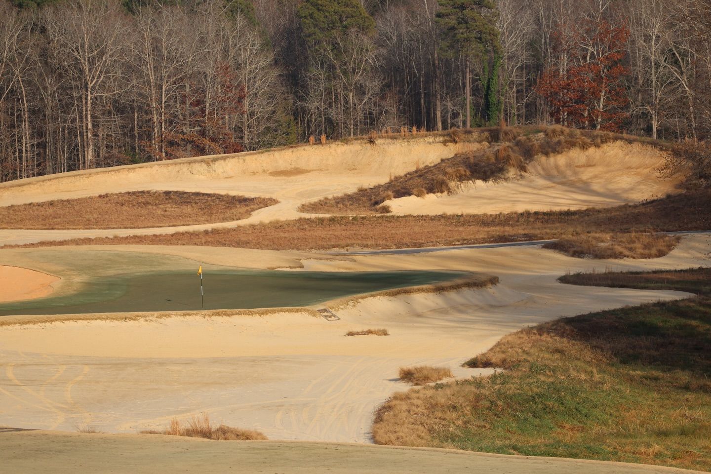 Golf course with sand bunkers, green, and bare trees.
