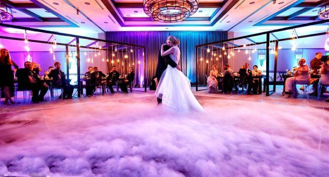 A bride and groom are dancing on a cloud in a large room.