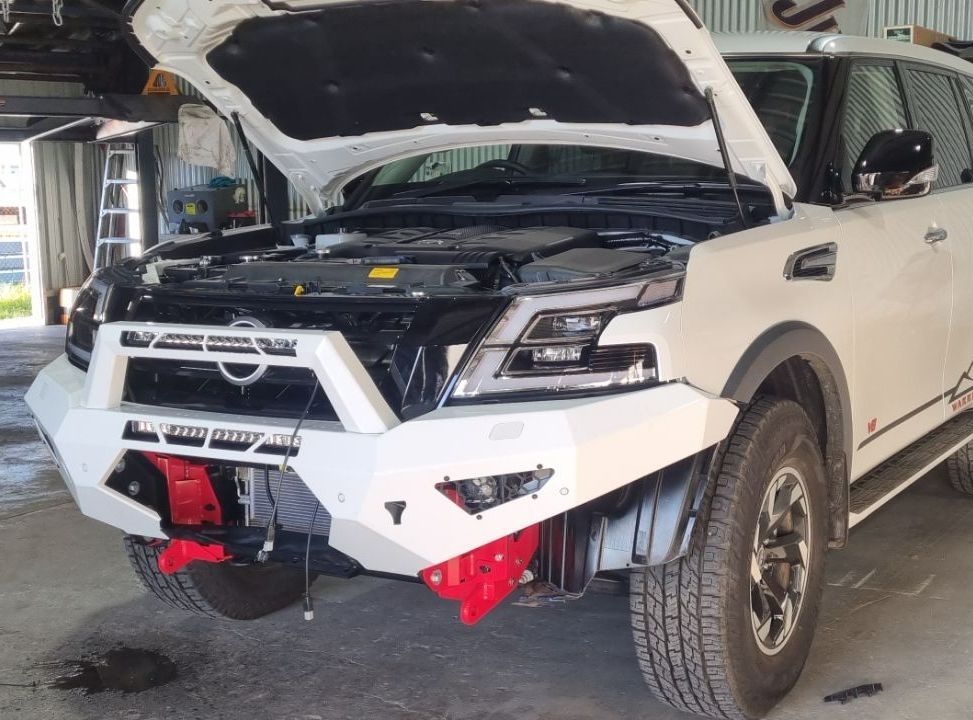 White Nissan Suv With Open Hood, Custom Front Bumper, And Red Tow Points In A Repair Shop