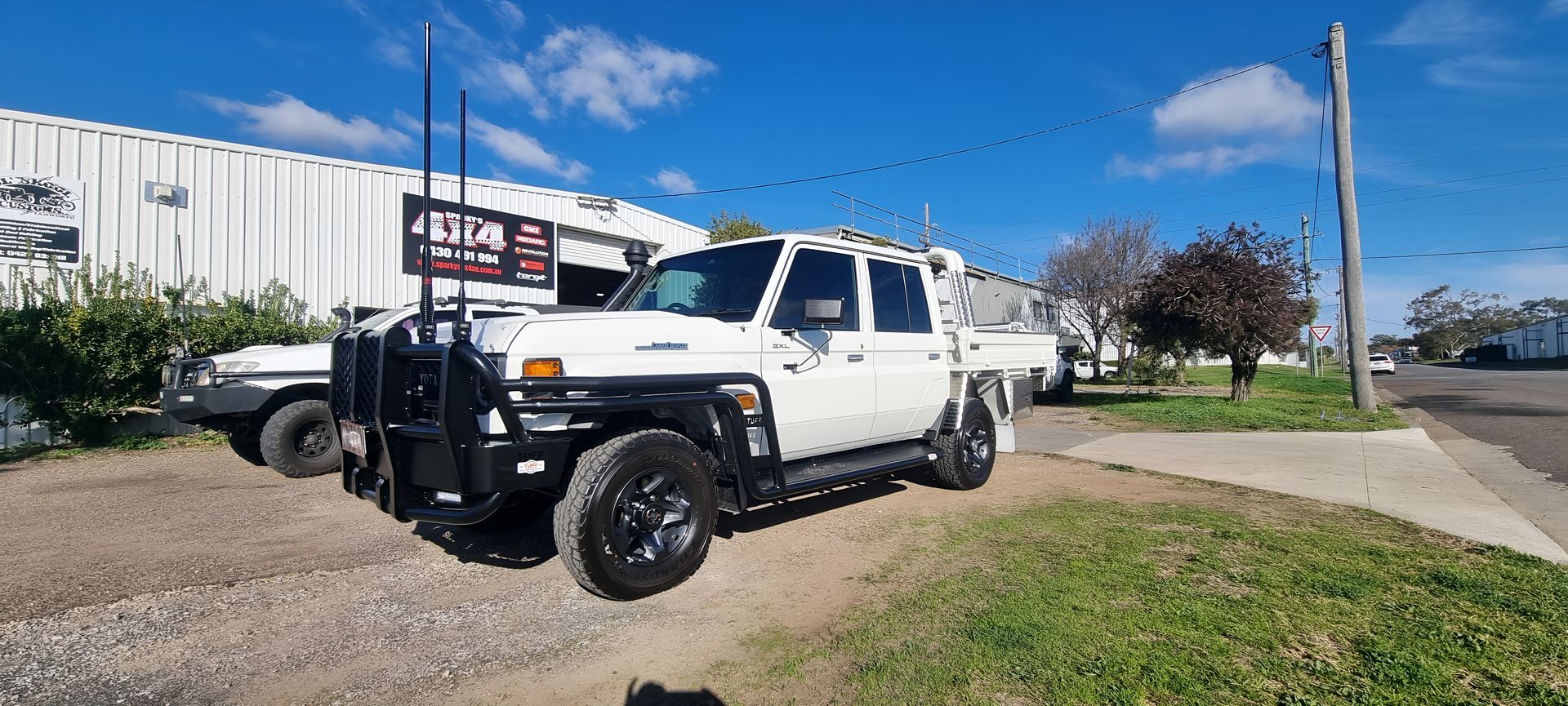 White Toyota LandCruiser 79 Series dual cab with bull bar and aerials parked outside workshop.