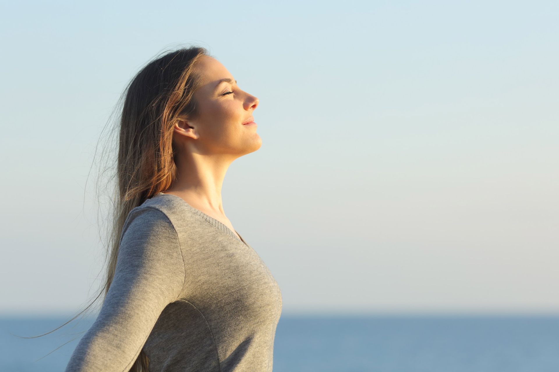 A woman is standing on the beach with her arms outstretched and her eyes closed.