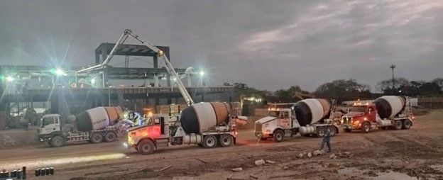 Una fila de hormigoneras circulan por un camino de tierra por la noche.