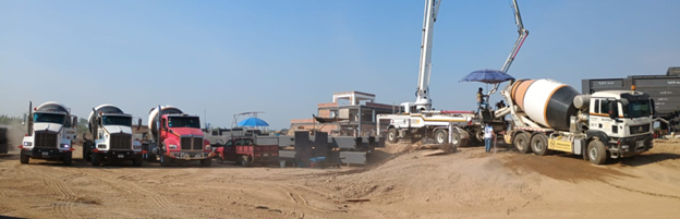 Una fila de camiones de hormigón está estacionada en un campo de tierra.
