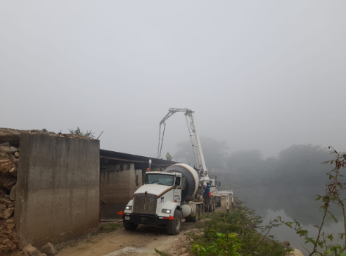 Un camión blanco circula por un camino de tierra junto a una masa de agua.