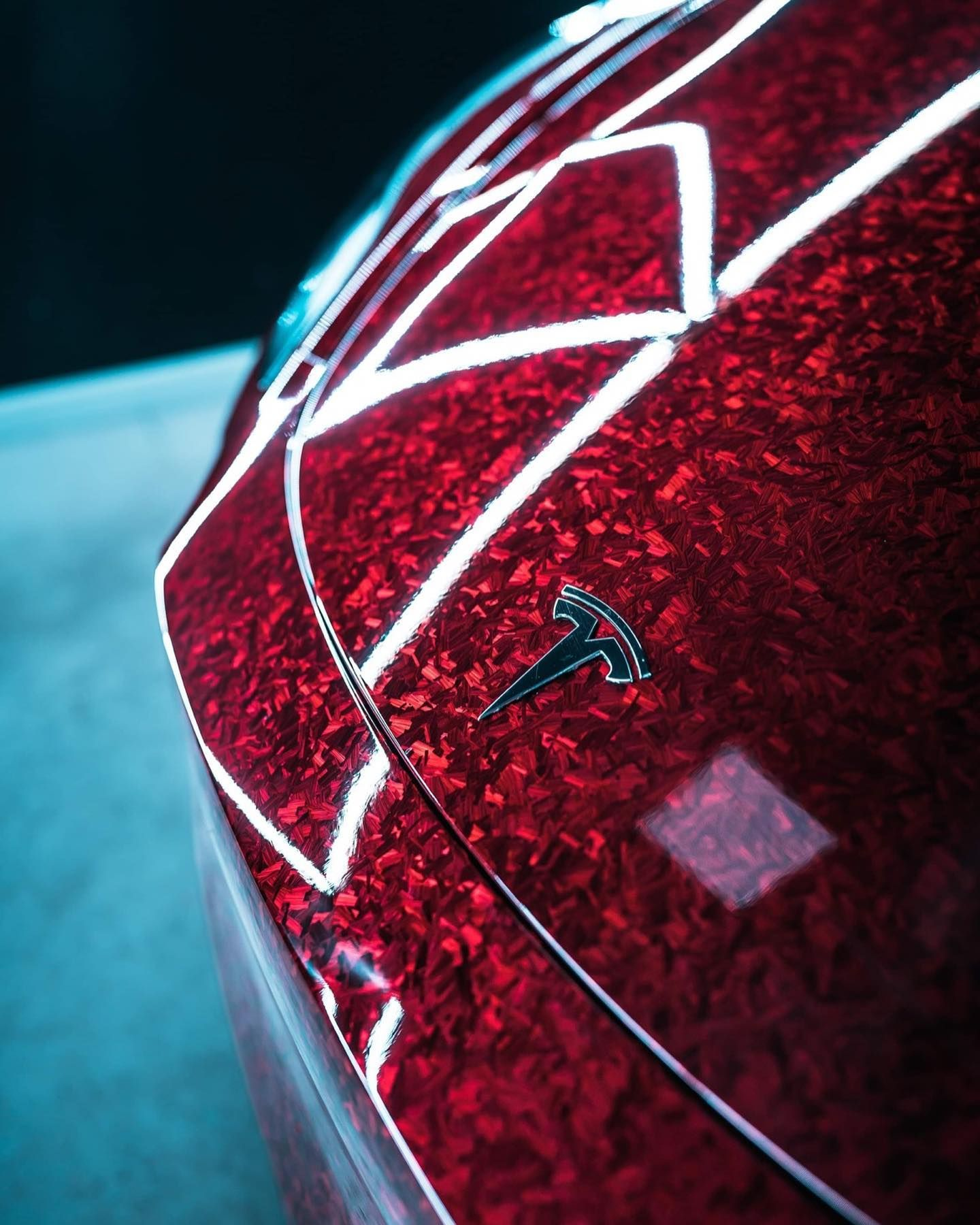 Close-up of a red glittery car surface with white geometric lines and a small Tesla logo