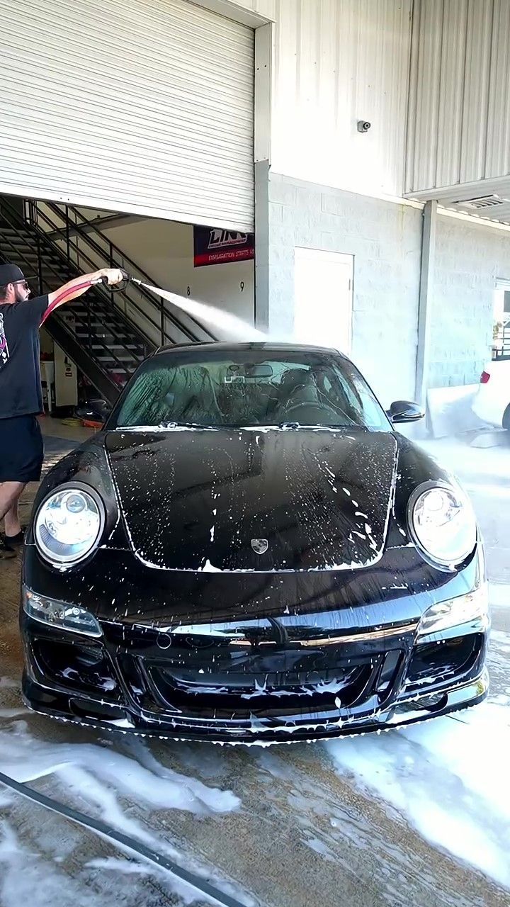 Professional auto detailer rinsing a black Porsche 911 during a foam wash as part of a full paint correction and ceramic coating service in Orlando.