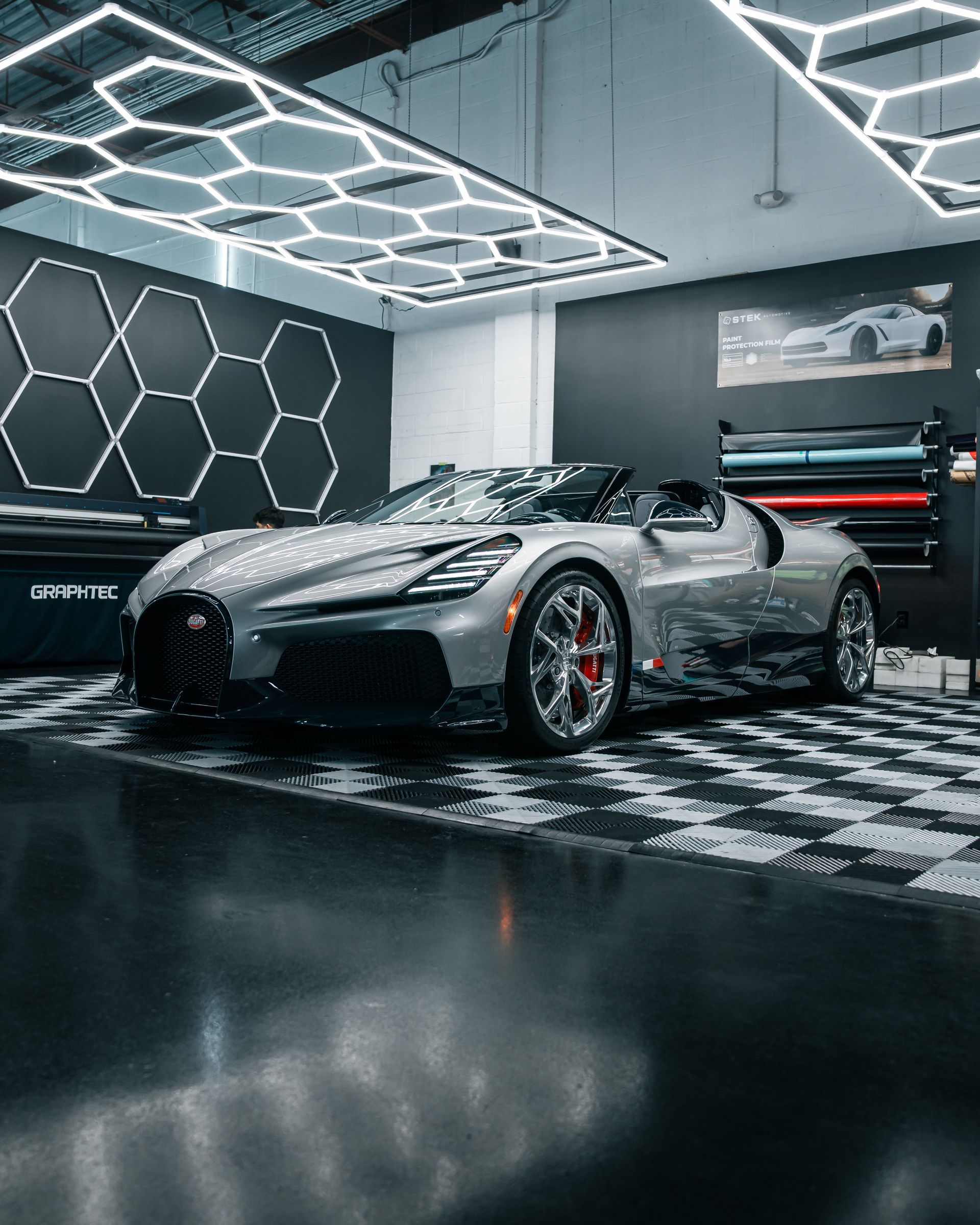 Silver sports car in a modern showroom with geometric ceiling lights and dark glossy flooring