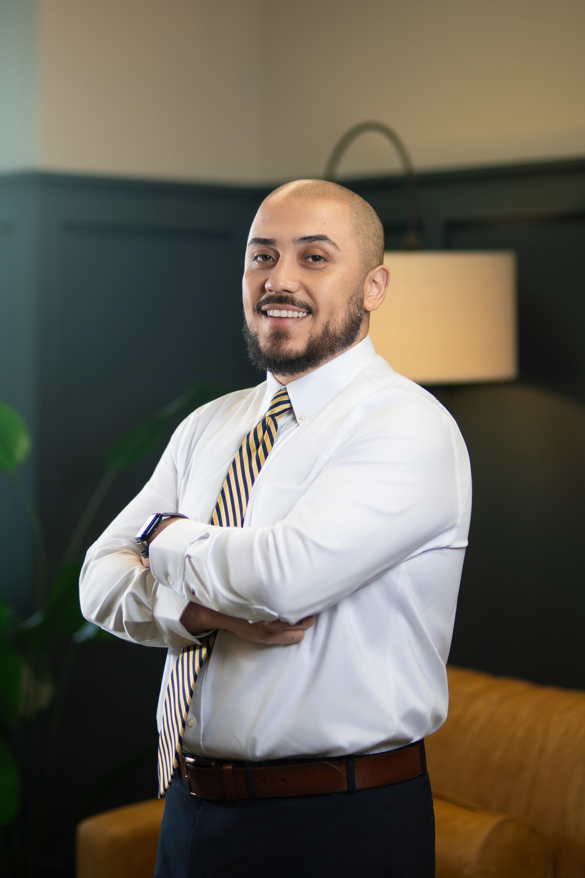 Smiling man with folded arms in a white shirt and striped tie, standing in an office lounge.