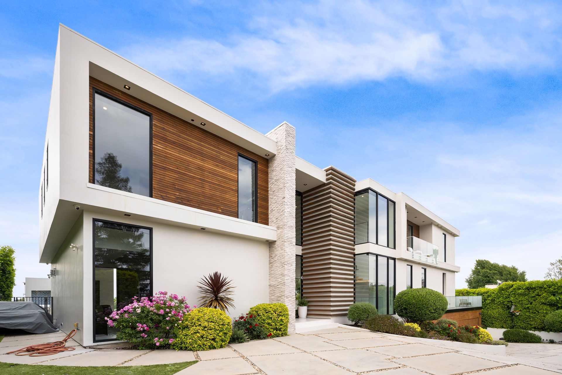 Modern white two-story house with wood accents, large windows, and a landscaped front yard under a blue sky