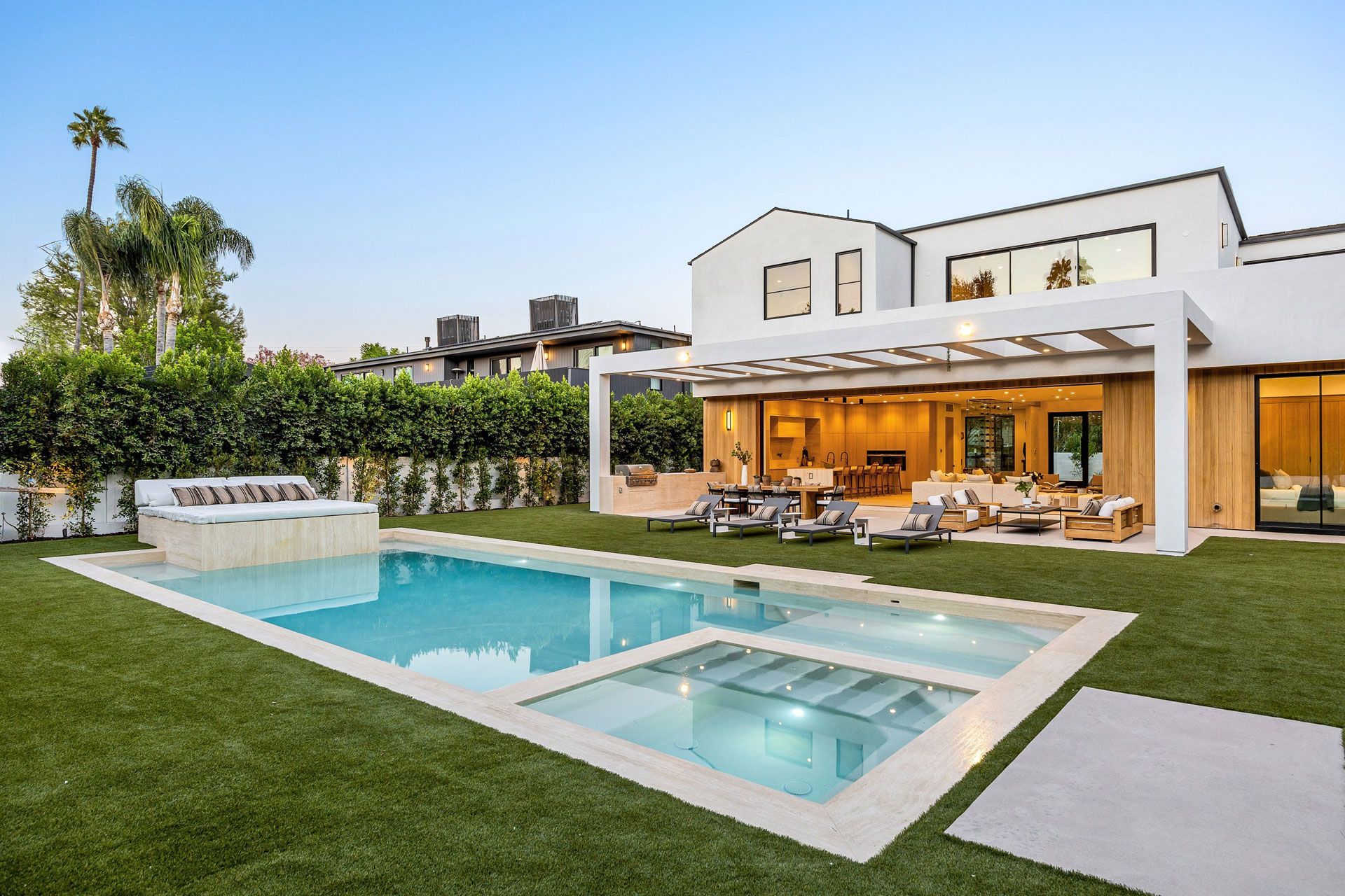 Modern luxury home with a lit patio, swimming pool, and manicured lawn at dusk