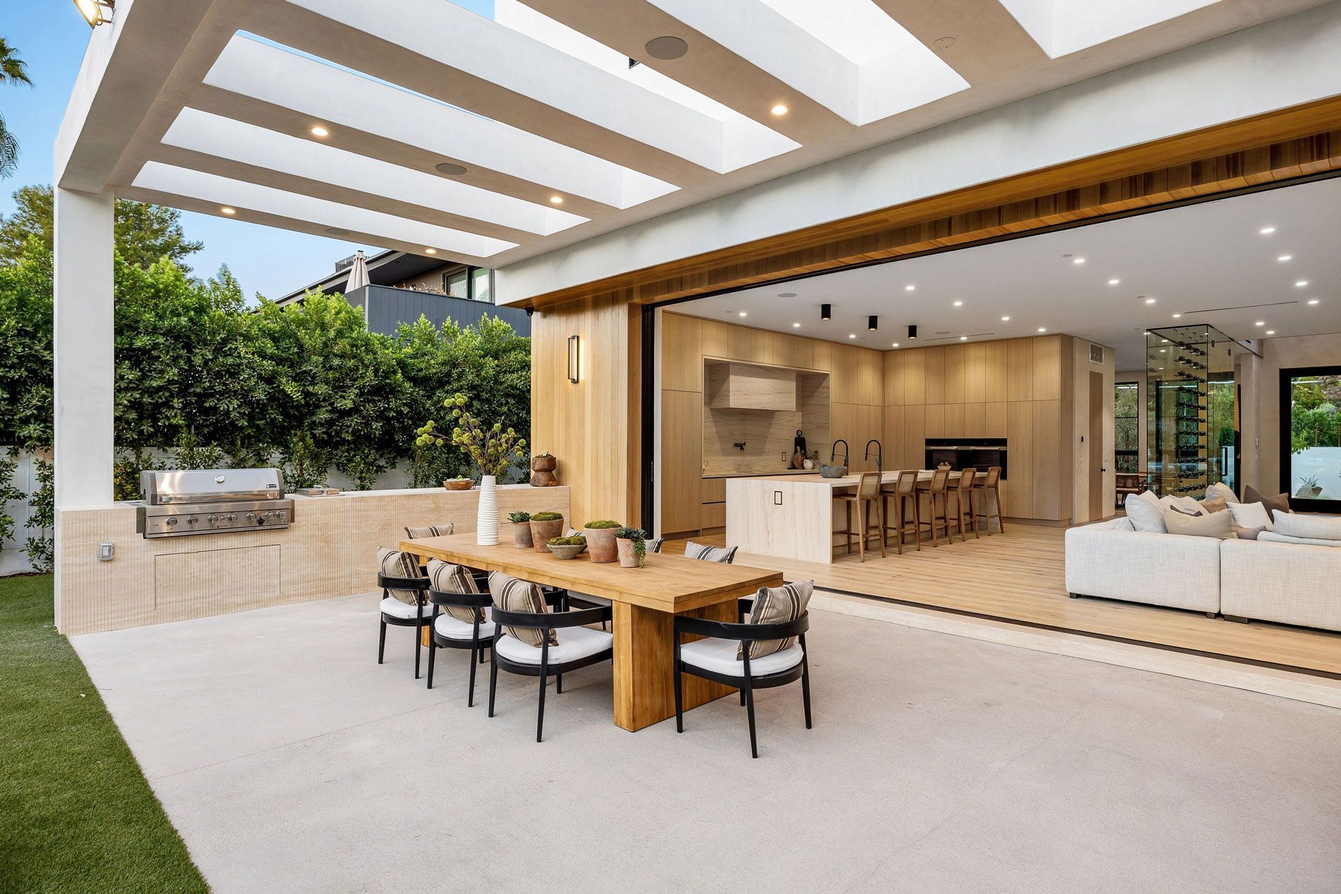 Modern outdoor patio with wooden dining table, built-in grill, and open view to a bright living room