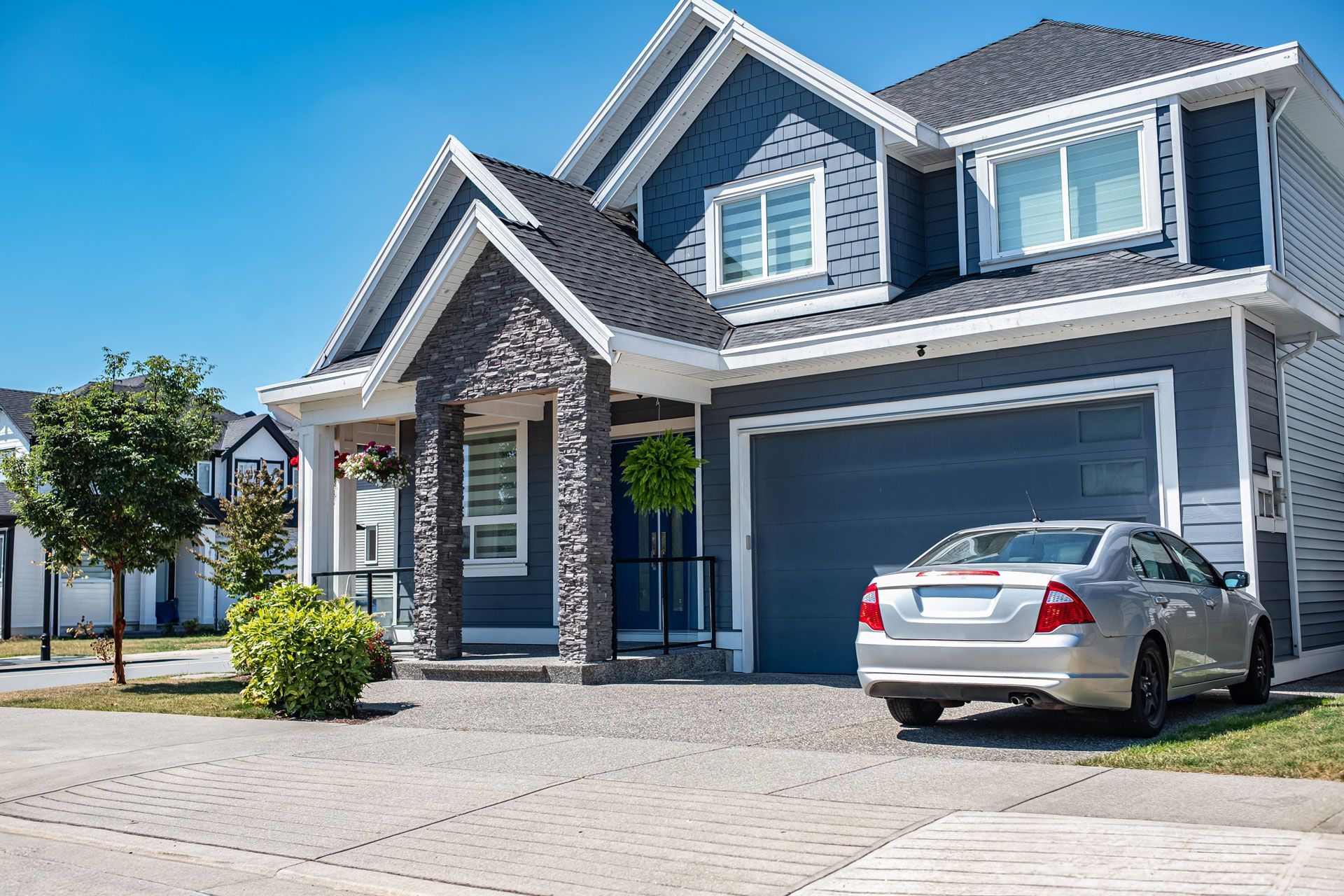 Modern gray two-story house with a silver car parked in the driveway under a clear blue sky