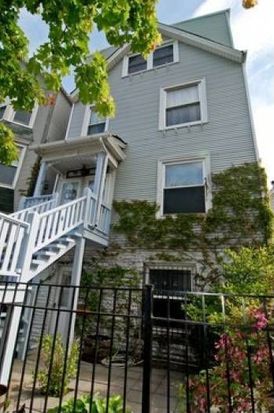 A large house with a staircase leading up to the second floor is behind a fence.