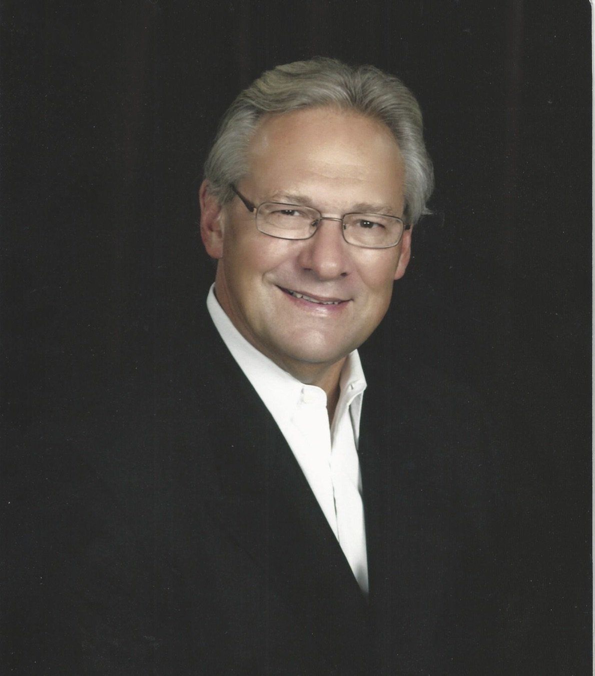 A man wearing glasses and a suit is smiling for the camera