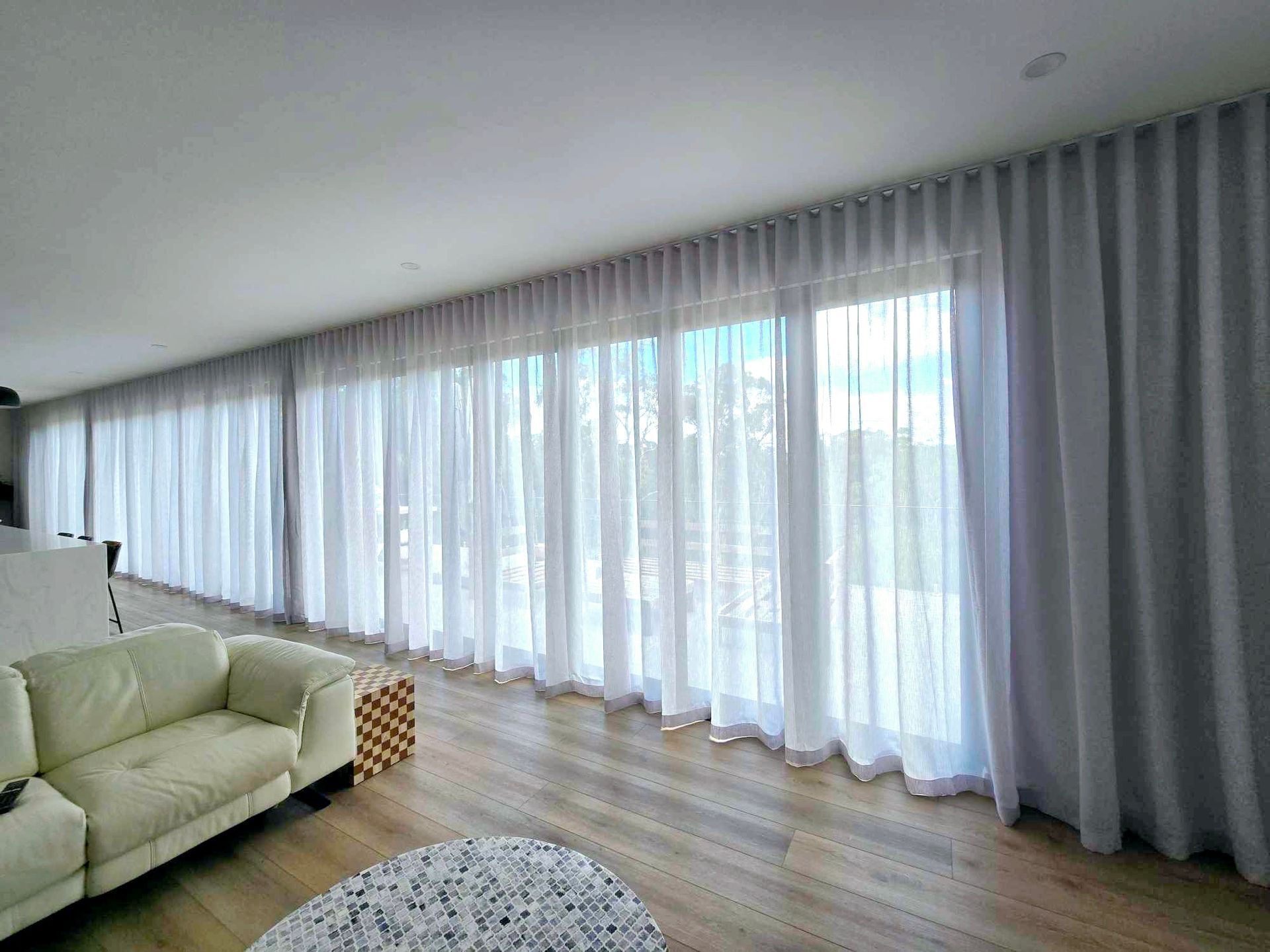 A living room with a couch , chair , and large windows with white curtains.