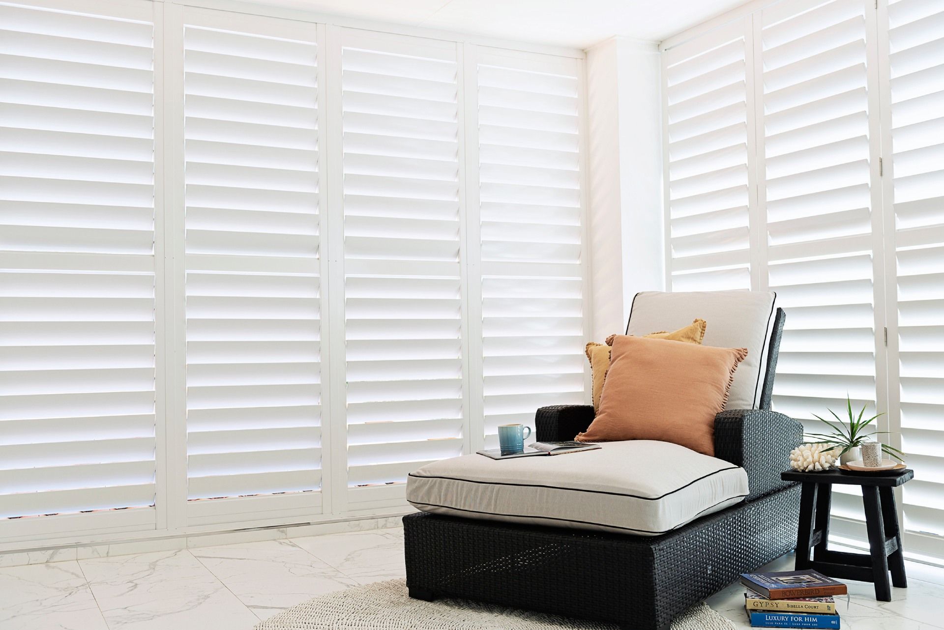 A chair is sitting in a living room with white shutters on the windows.