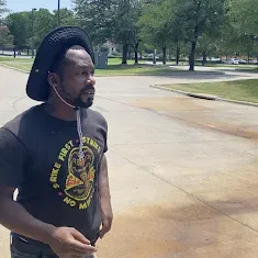 Man in a black Cobra Kai t-shirt and hat outside, looking to the side.
