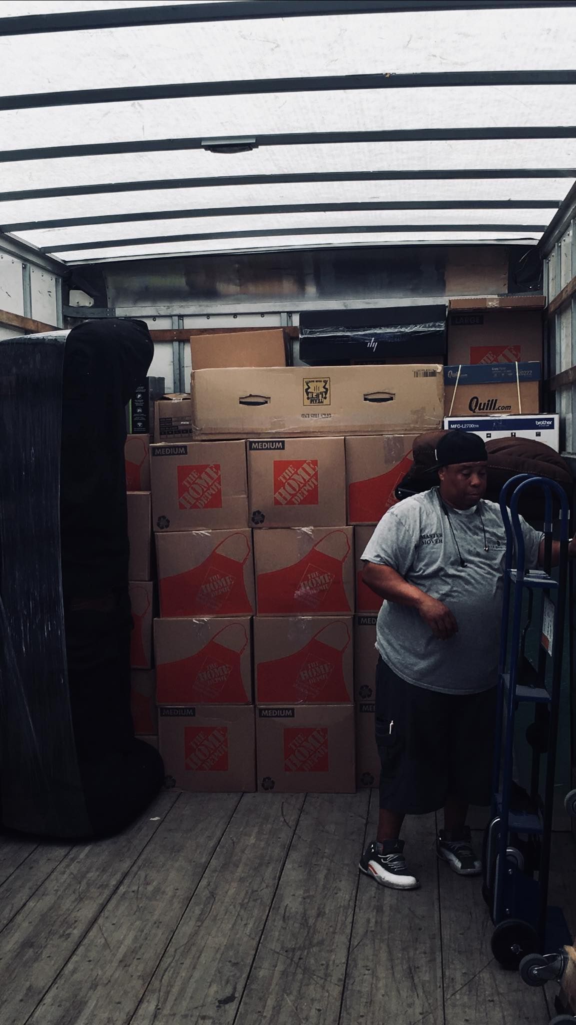 Man loading boxes into a truck. Inside the truck are stacks of cardboard boxes, and a furniture dolly is to his right.