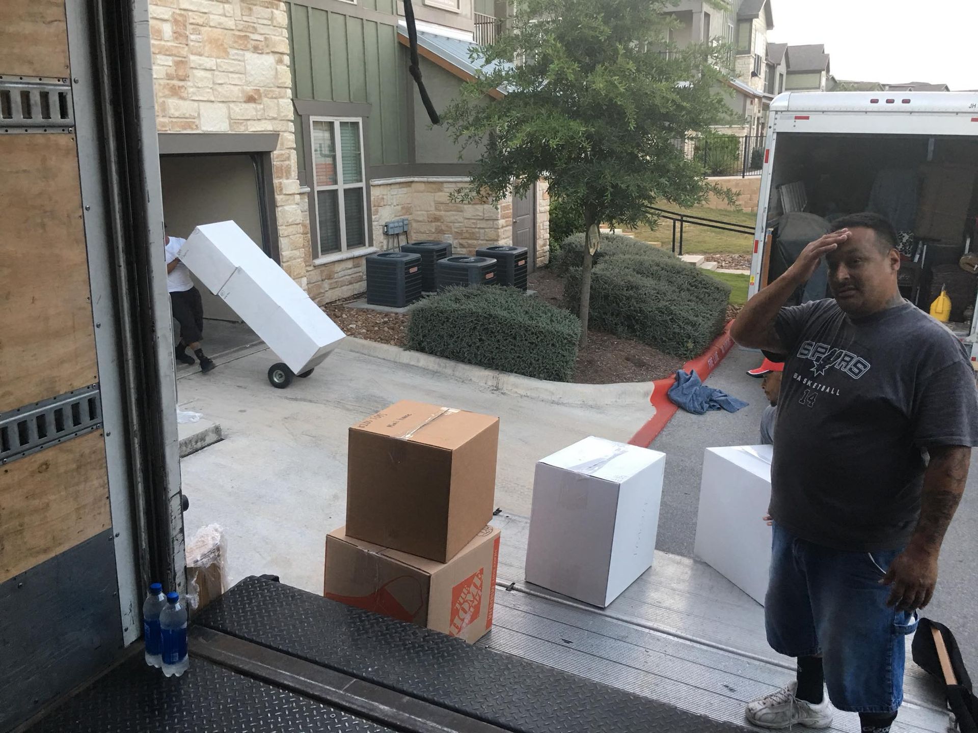 Movers unloading boxes from a truck on a driveway. Man wiping sweat from his forehead.