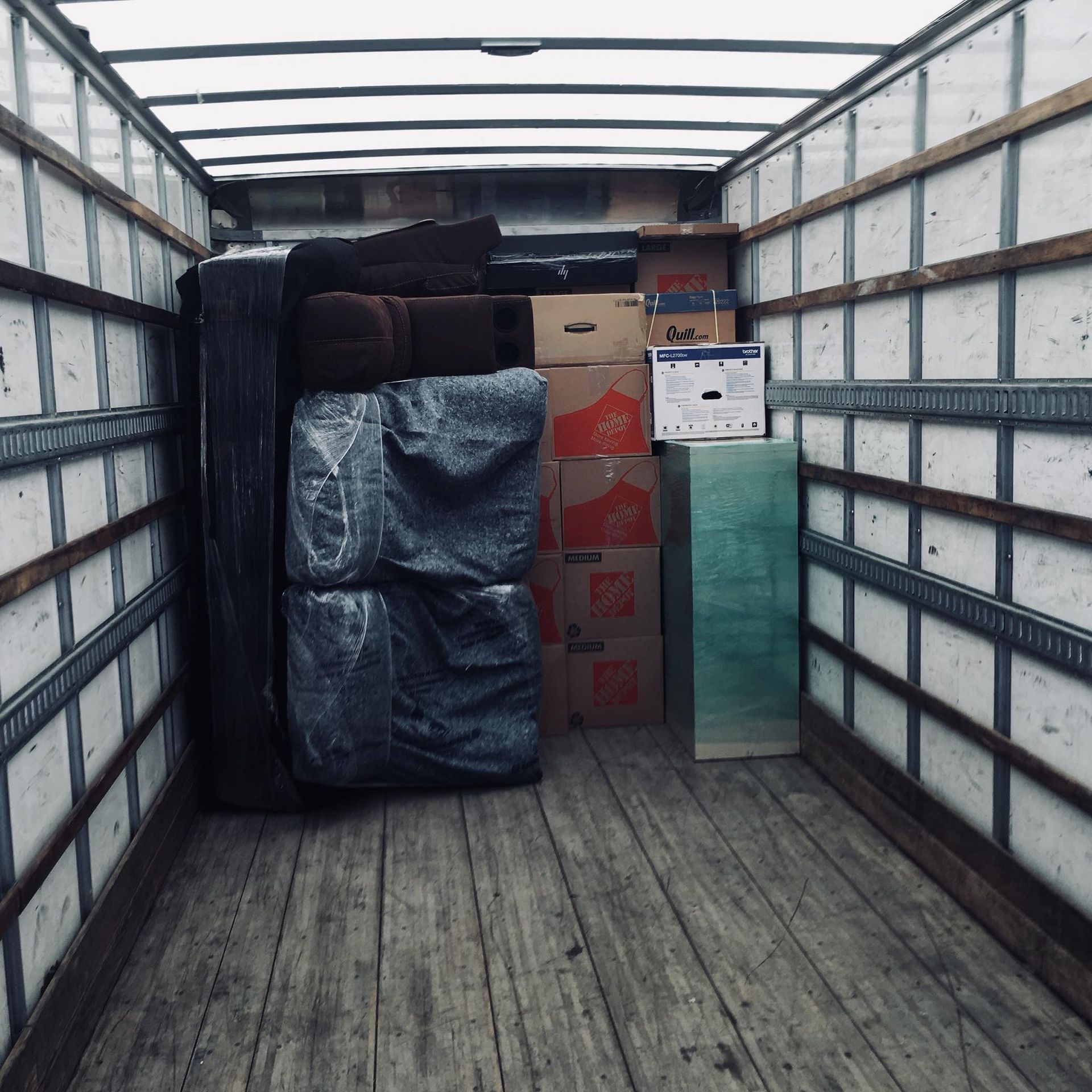 Interior of a moving truck filled with furniture and boxes. The floor is wood, the walls are white.