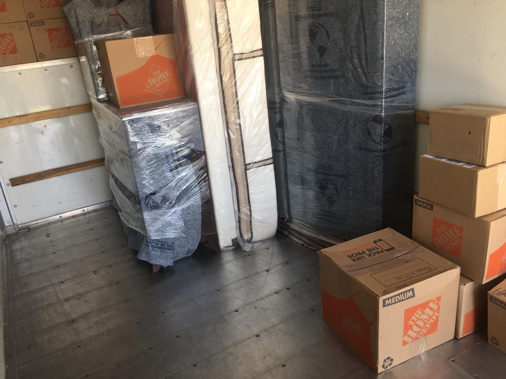 Boxes and furniture wrapped in plastic inside a moving truck.
