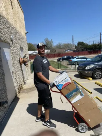 Man with a top knot cutting open a cardboard box with a utility knife.