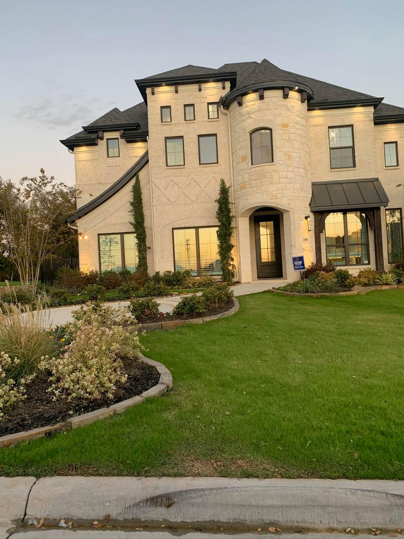 Large stone house with a dark roof, manicured lawn, and landscaping.